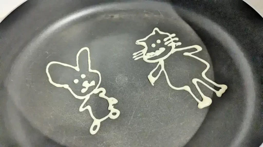 フライパンにパンケーキの生地で絵を描いたところ。この後生地で埋める